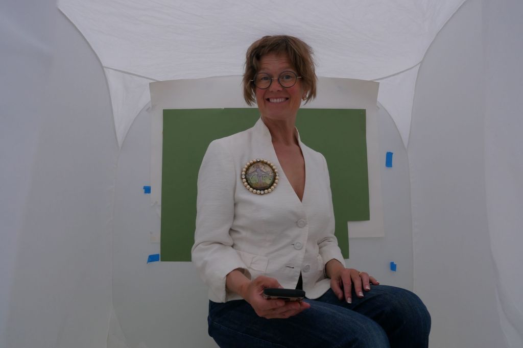 Picture of a woman sat in a small white photo tent wearing jeans and a cream top and wearing a large cast glass, engraved and enamelled essex crystal brooch