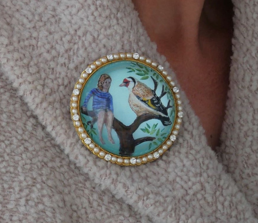 Reverse intaglio cast glass, carved and enamel painted crystal showing a large goldfinch alongside a small girl, both in a tree